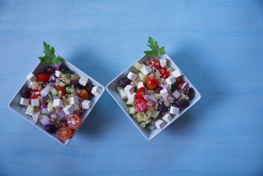 Greek salad in square plates with cherry tomatoes, black olives, onion and cheese, on a light blue background.