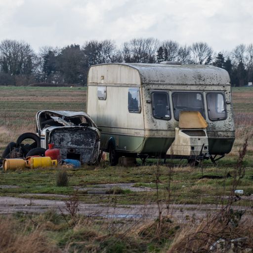 An old abandoned camper trailer, some gas tanks and old tires on an abandoned lot