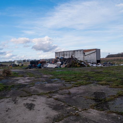 An abandoned lot with a pile of burned trash, discarded furniture and an old camper trailer