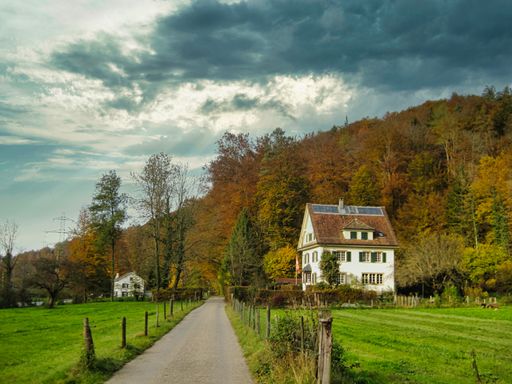 A walking trail with houses going to the mountains and forests on a cloudy day