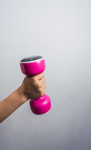 A hand of a Caucasian boy lifting a pink dumbbell, isolated against silver background.