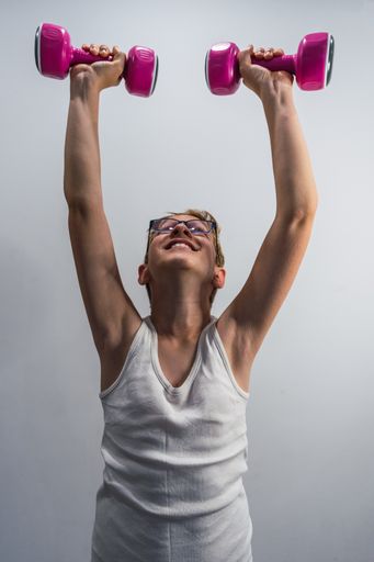 A young happy Caucasian boy in sportswear, lifting light dumbbells, isolated silver background