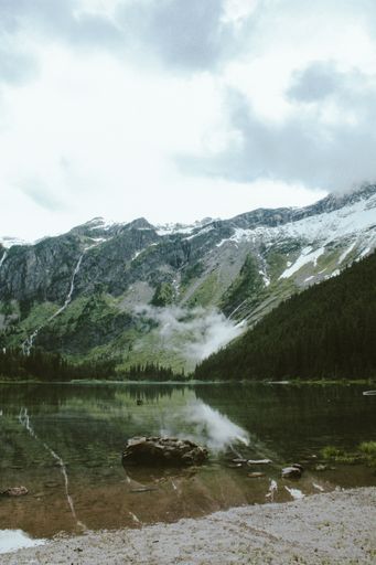 A vertical shot of a rock in Avalanche Lake, with a forested mountain in the background at Glacier National Park, Montana, USA