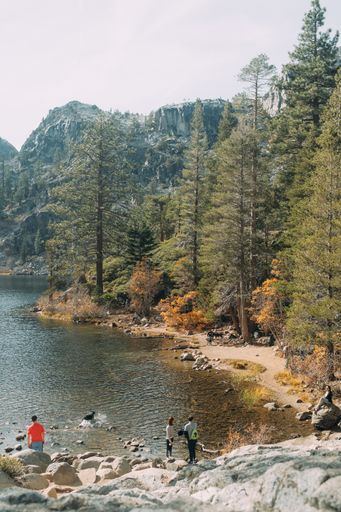A vertical shot of people standing and sitting on rocks near water and tall trees with a mountain in the distance in California, USA
