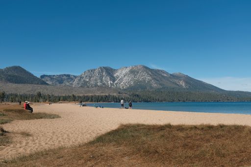 A wide shot of people walking and sitting on the Laake Tahoe shore with mountain and a blue sky in the background in  California, USA