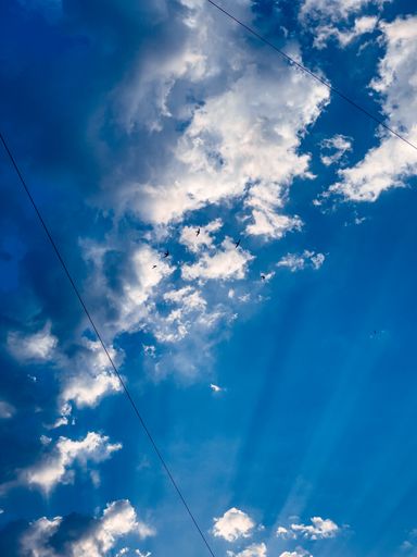 A vertical shot of the blue sky with white clouds and rays of sunshine