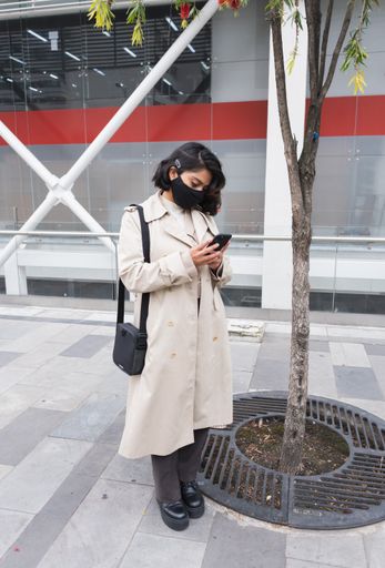 A vertical shot of a young professional female in a protective mask using the phone
