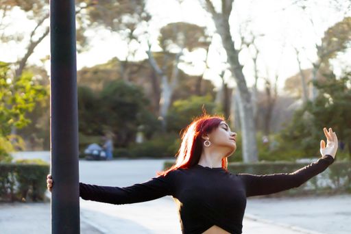 A beautiful red haired ballerina gracefully dancing at a park with soft sunlight in the background