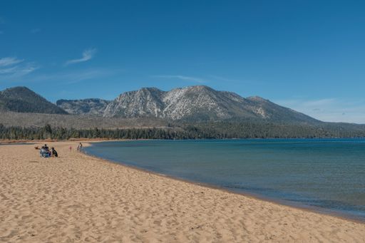 A wide shot of people sitting near the LakeTahoe shore with a mountain in the distance at California