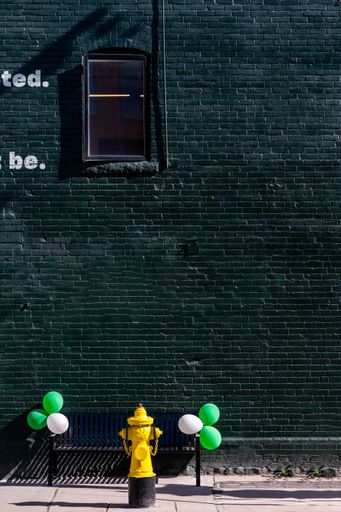 A vertical shot of a brick building wall painted in green and balloons in tone placed closeby