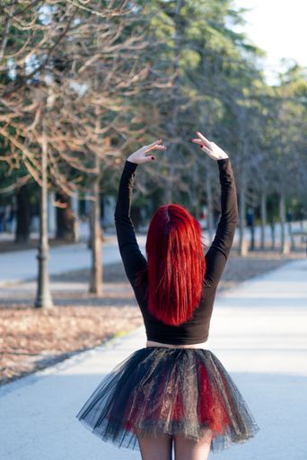 A beautiful red haired ballerina gracefully dancing at a park with trees in the background