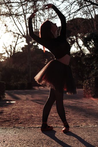 A silhouette of a ballerina gracefully dancing at a park with trees in the background
