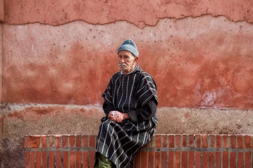 A man seated on a brick bench by graffiti wall