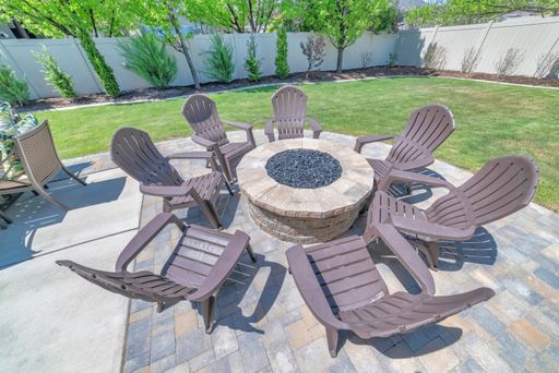 A backyard fire pit made of brick on the deck of a home with chairs set up around it
