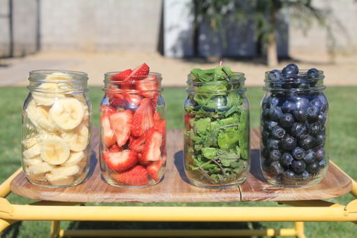 A closeup of bananas, strawberries, mint leaves, and blackberries in glass jars on a wooden chair