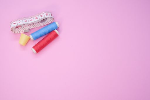 A closeup of the colorful  sewing threads with a thimble and a measuring tape on the pink surface