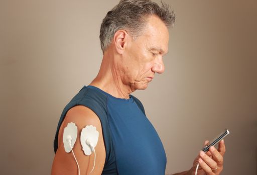 A man using an Electro Therapy Massager or Tens Unit on his Deltoids muscle for pain relief for Muscles and Joints