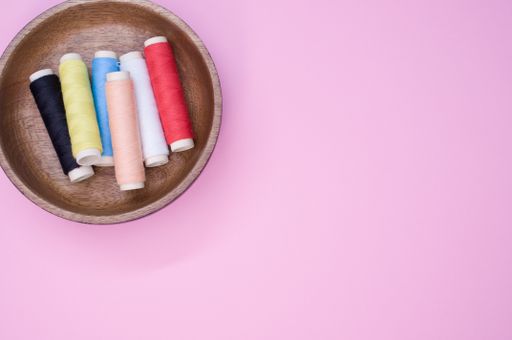 A top view of the colorful sewing threads in the wooden bowl on the pink surface