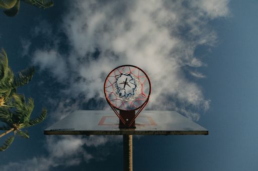 An upshot of a basketball hoop with an airplane visible through the basket hole in the sky