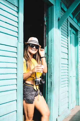 vertical portrait of a young female traveler photographer with glasses holding an ice cold drink. travel concept.