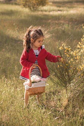 A little girl standing in a field holding a flower basket with a blurred background