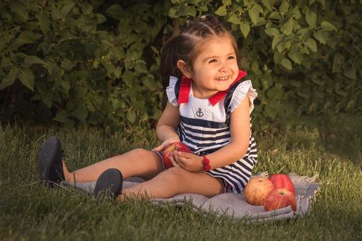 A sitting little girl holding an apple cheerfully looking at the right