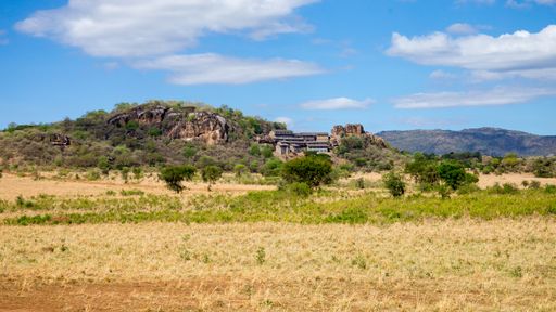 A beautiful view of a home set on a rocky hillside with dry grass field in the foreground