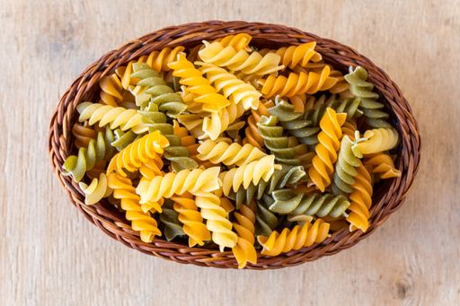 A top view of raw three colors Rotini pasta in a wooden bowl