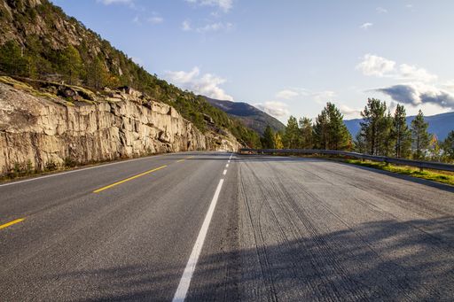 A high angle shot of an empty road in Norway surrounded by trees and hills