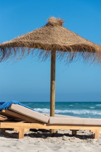 A vertical shot of a deck chair and a straw umbrella on the wonderful island of Formentera in Spain