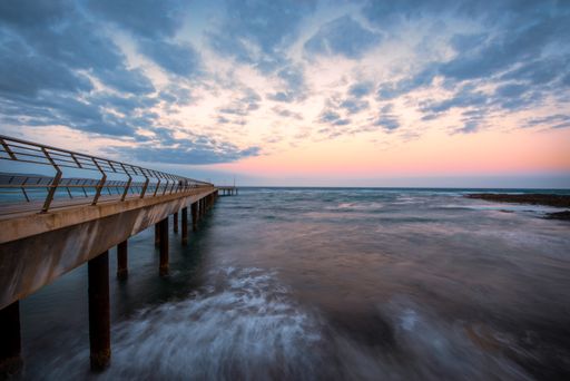 A closeup shot of a long pier in the sea and the colorful skyline during sunset