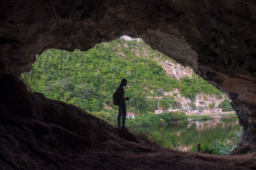 A Silhouette view of a Hispanic man with backpack wearing black face mask photo shooting inside a dark cave in Matanzas city Cuba