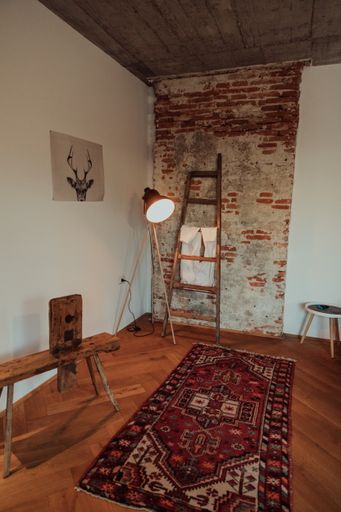 A vertical shot of a loft-stye room with a wooden bench, stair and a colorful carpet