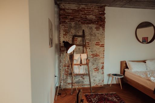 an interior of a loft-style bedroom with a wooden bed and colorful carpets