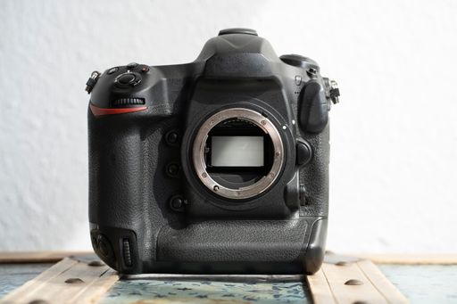A closeup of a full-format photographic camera agaisnt a white wall