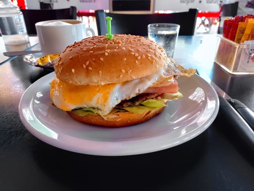 shot of a complete hamburger or ground meat burger with egg, cheese, ham tomato and lettuce in a plate on a dark wooden table