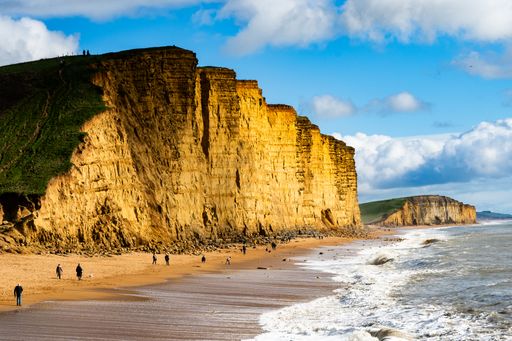 The people strolling on a beach near yellow cliffs at Jurassic coast