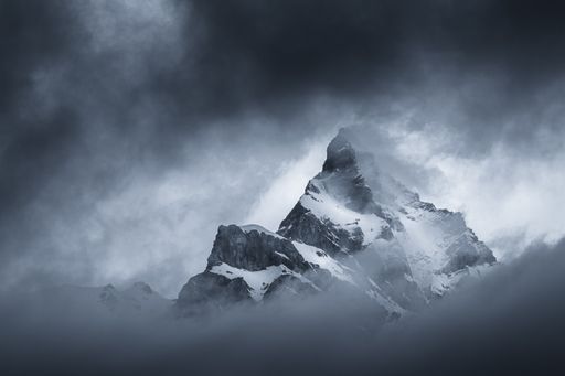 Moody black and white landscape view of a mountain appearing in the dark clouds at sunrise