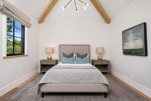 Master bedroom with wooden beamed ceiling, grey bed, and white walls
