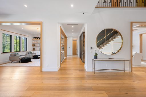 Spacious, pristine foyer with white walls, wooden floors, and a round chandelier