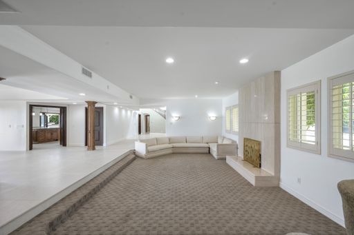 A spacious living room with oversized carpet, neutral couches, and cozy fireplace in Encino, California