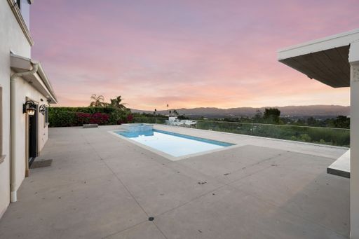 A spacious pool by a white house with green trees in the distance