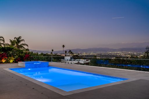 An empty swimming pool with city lights in the distance under a clear blue sky