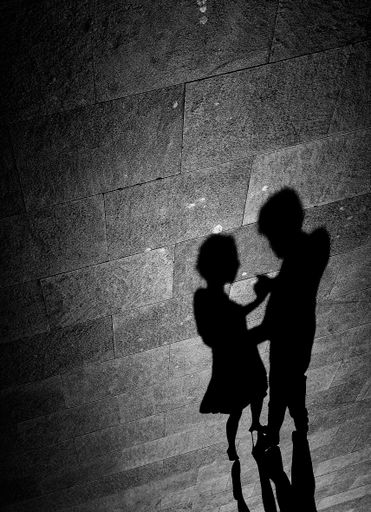 A grayscale shot of a shadow on the ground of a romantic pair dancing