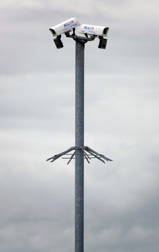 Two Aceda security cameras mounted on a high metal pole in an outdoor setting against a cloudy background.