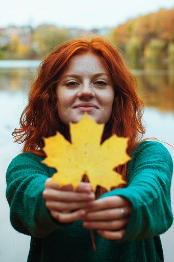 A young redhead woman holding a yellow leaf in autumn
