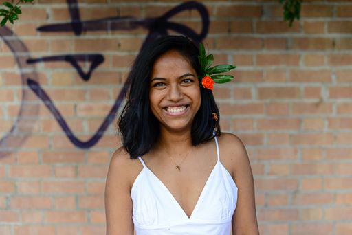 A young cheerful East Asian female wearing a beautiful white dress standing against a brick wall