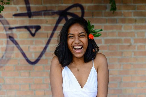 A young cheerful East Asian female wearing a beautiful white dress standing against a brick wall