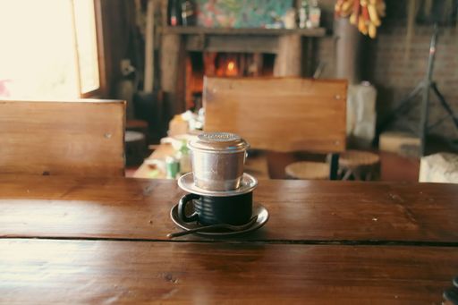 Traditional Vietnamese coffee prepared by slow drip on a rustic wooden table with a lit cozy stone fireplace in the blurry background