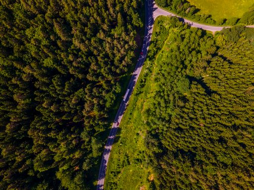 An aerial view of the asphalt road surrounded by green forests